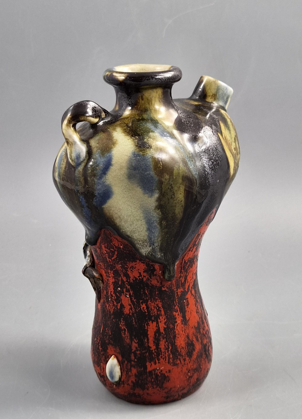 A Japanese Sumida Gawa pottery vase featuring an asymmetrical spouted form with a dark flambe drip glaze over a textured red lower body adorned with applied high-relief figures of boys. View IV