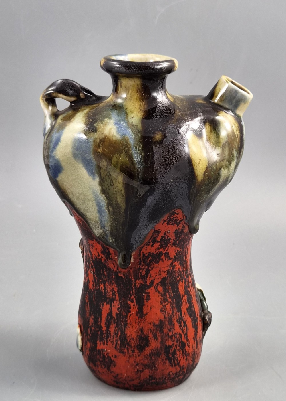 A Japanese Sumida Gawa pottery vase featuring an asymmetrical spouted form with a dark flambe drip glaze over a textured red lower body adorned with applied high-relief figures of boys. View V