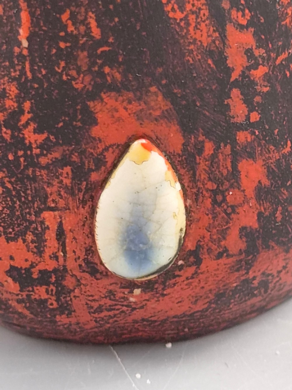 A Japanese Sumida Gawa pottery vase featuring an asymmetrical spouted form with a dark flambe drip glaze over a textured red lower body adorned with applied high-relief figures of boys. View X