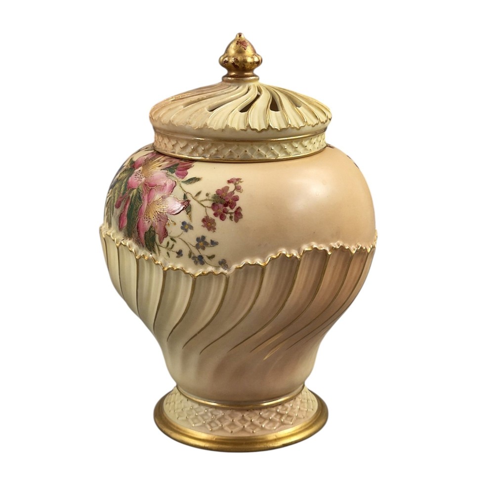 A Royal Worcester blush ivory porcelain pot-pourri jar with a pierced lid, fluted swirled lower body, gold trim, and hand-painted floral motifs. View II