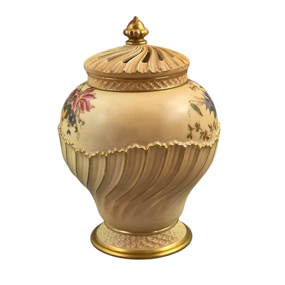 A Royal Worcester blush ivory porcelain pot-pourri jar with a pierced lid, fluted swirled lower body, gold trim, and hand-painted floral motifs. View V