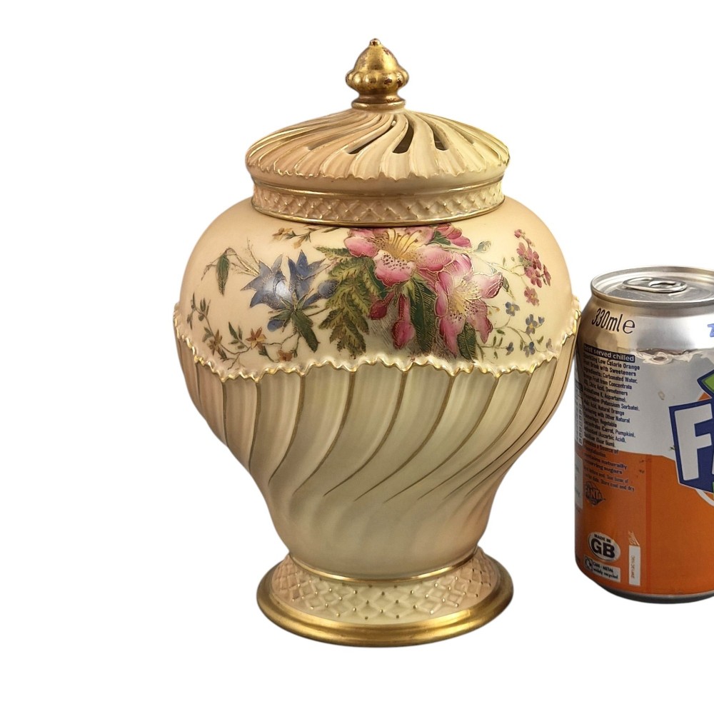 A Royal Worcester blush ivory porcelain pot-pourri jar with a pierced lid, fluted swirled lower body, gold trim, and hand-painted floral motifs. View VII