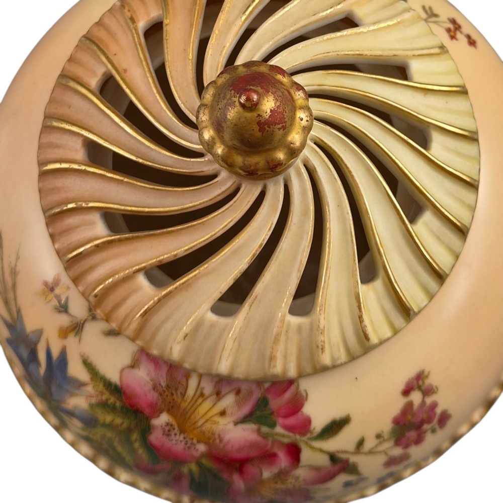 A Royal Worcester blush ivory porcelain pot-pourri jar with a pierced lid, fluted swirled lower body, gold trim, and hand-painted floral motifs. View VIII