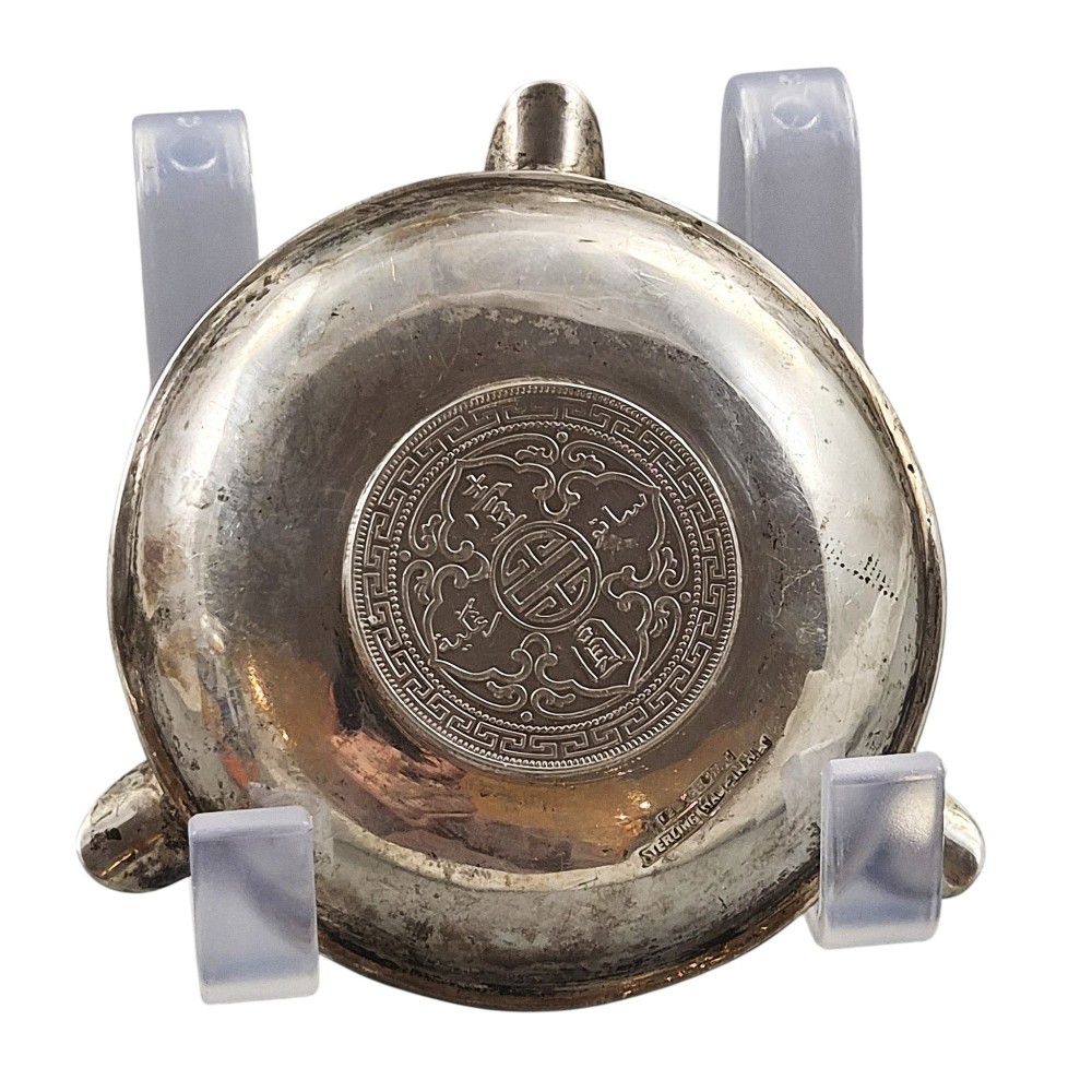 A circular sterling silver dish featuring three cigarette rests on the outer rim and an inset 1899 British Trade Dollar coin in the centre. View III