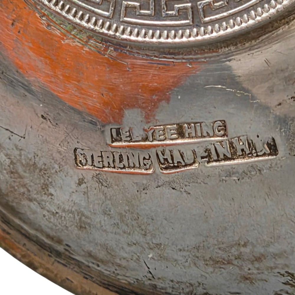 A circular sterling silver dish featuring three cigarette rests on the outer rim and an inset 1899 British Trade Dollar coin in the centre. View VI