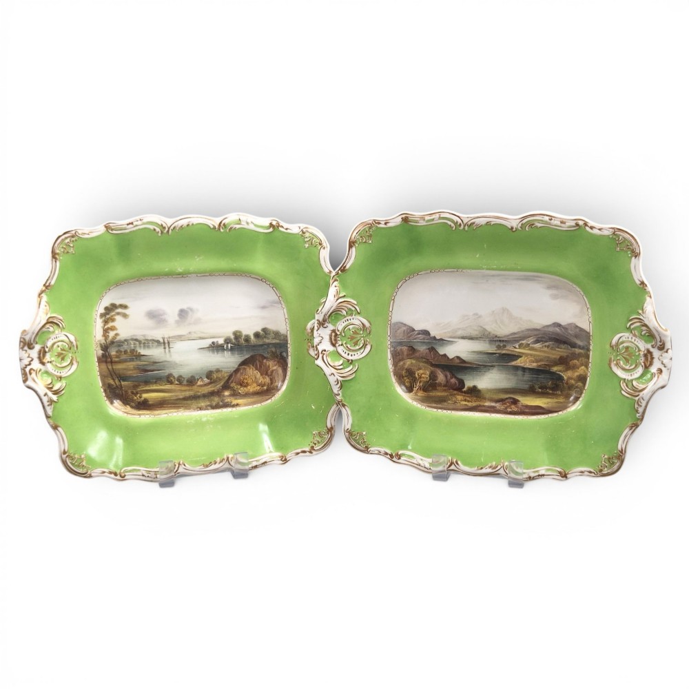 A pair of rectangular porcelain serving dishes featuring apple green borders with gilded scrollwork and central hand-painted landscape scenes.