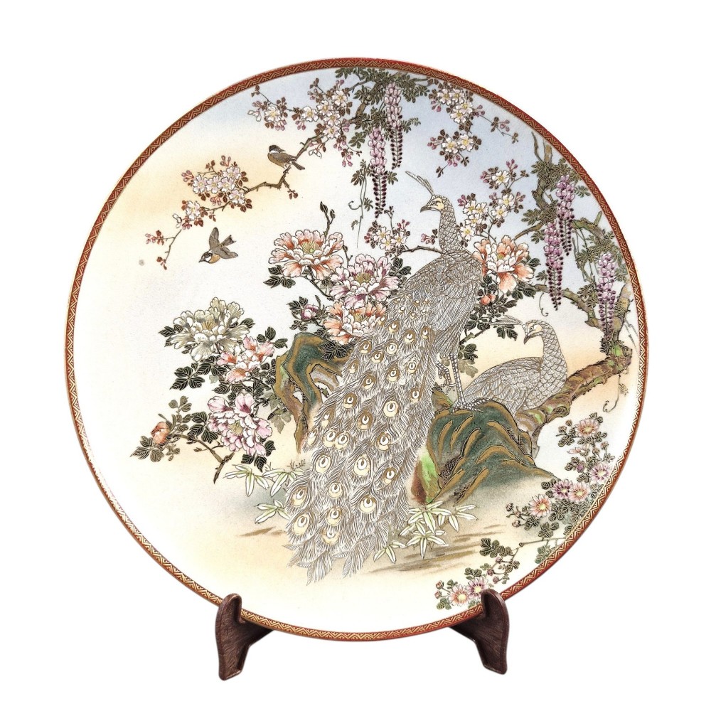 A large circular Japanese Satsuma ceramic charger featuring raised enamel illustrations of peacocks, wisteria, and peonies on a cream crackle glaze background.