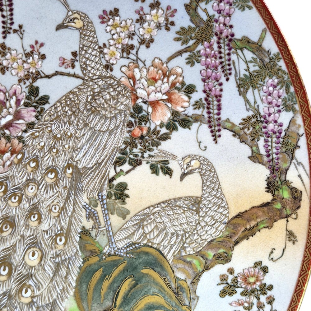 A large circular Japanese Satsuma ceramic charger featuring raised enamel illustrations of peacocks, wisteria, and peonies on a cream crackle glaze background. View IV