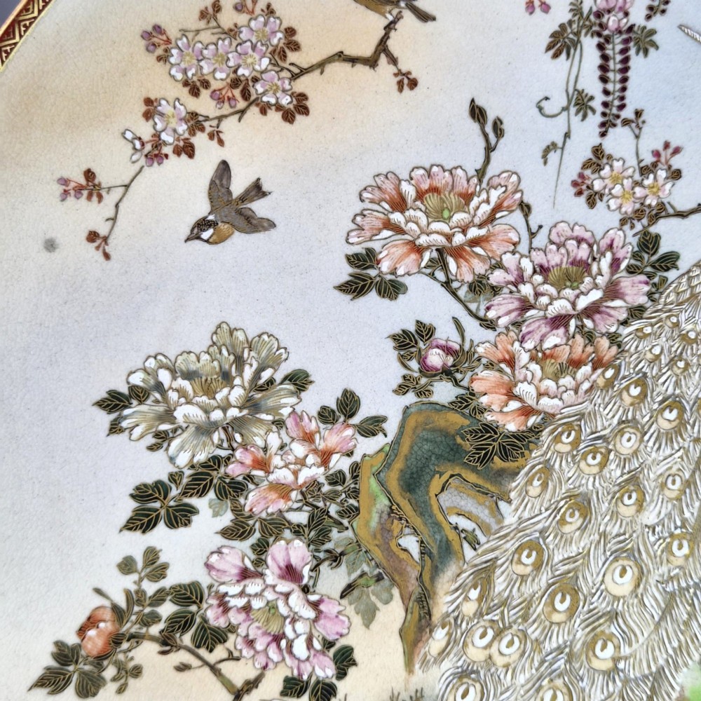 A large circular Japanese Satsuma ceramic charger featuring raised enamel illustrations of peacocks, wisteria, and peonies on a cream crackle glaze background. View VI