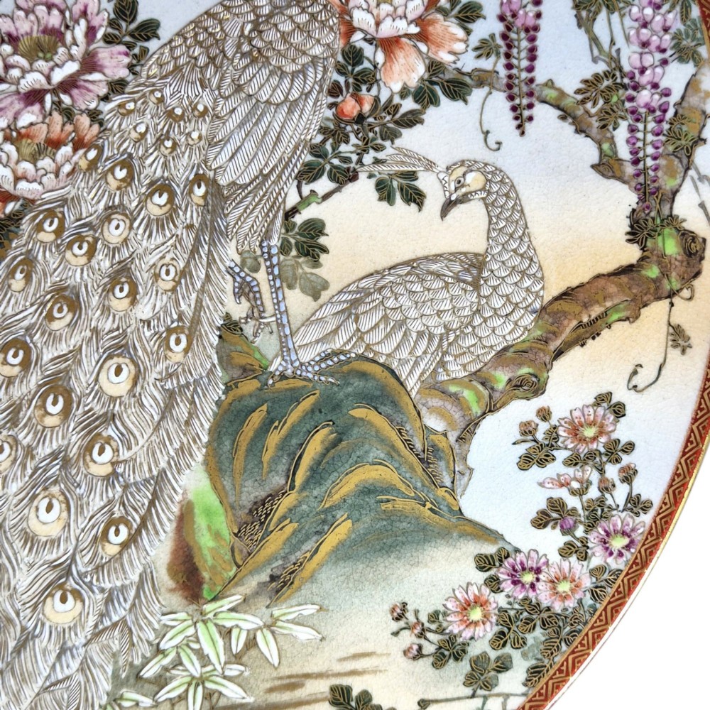 A large circular Japanese Satsuma ceramic charger featuring raised enamel illustrations of peacocks, wisteria, and peonies on a cream crackle glaze background. View VII