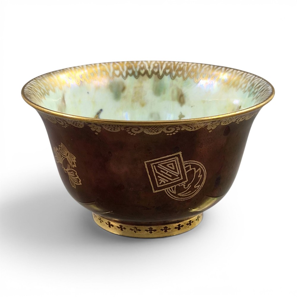 A deep red ceramic bowl with a flared rim, featuring gilded motifs on the exterior and an iridescent opalescent glazed interior.