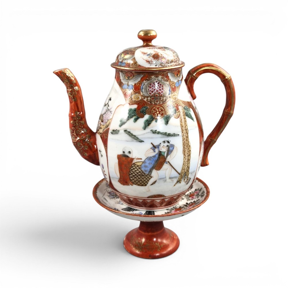 A Japanese Kutani porcelain teapot decorated with iron-red enamel, gilded accents, and hand-painted figurative scenes, seated on a matching pedestal stand.