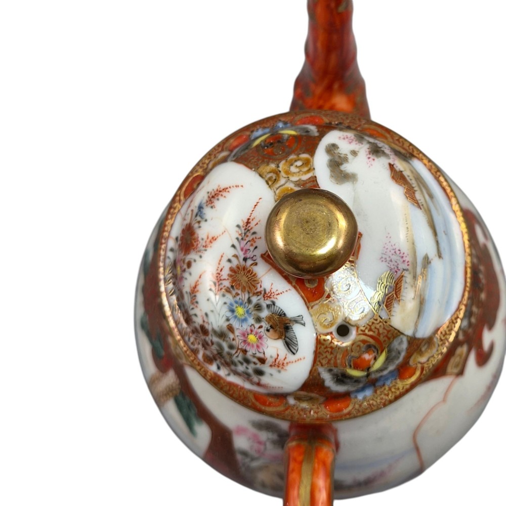 A Japanese Kutani porcelain teapot decorated with iron-red enamel, gilded accents, and hand-painted figurative scenes, seated on a matching pedestal stand. View X