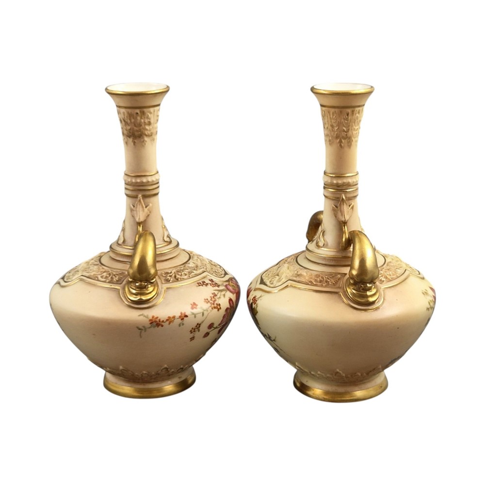 A symmetrical pair of Edwardian Royal Worcester blush ivory porcelain vases featuring gilded dolphin handles, relief-moulded necks, and hand-painted floral decoration. View IV