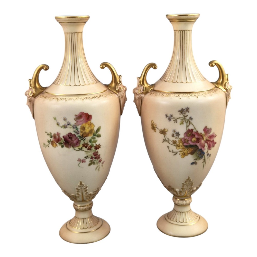 A pair of Royal Worcester blush ivory porcelain urn-shaped vases featuring hand-painted floral motifs, gold-gilded handles, fluted necks, and circular pedestal bases. View III