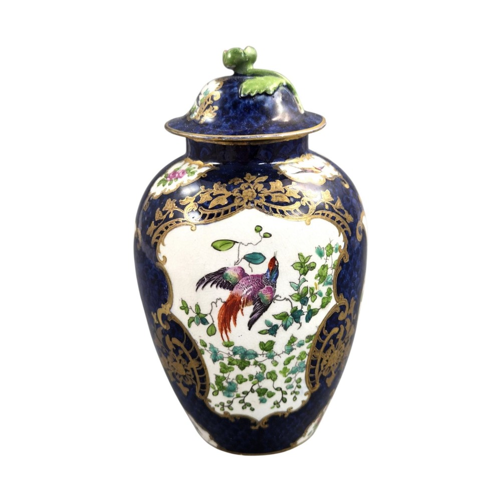 An Edwardian covered ceramic vase featuring a dark scale blue ground with gilded rococo cartouches framing painted floral panels. View II