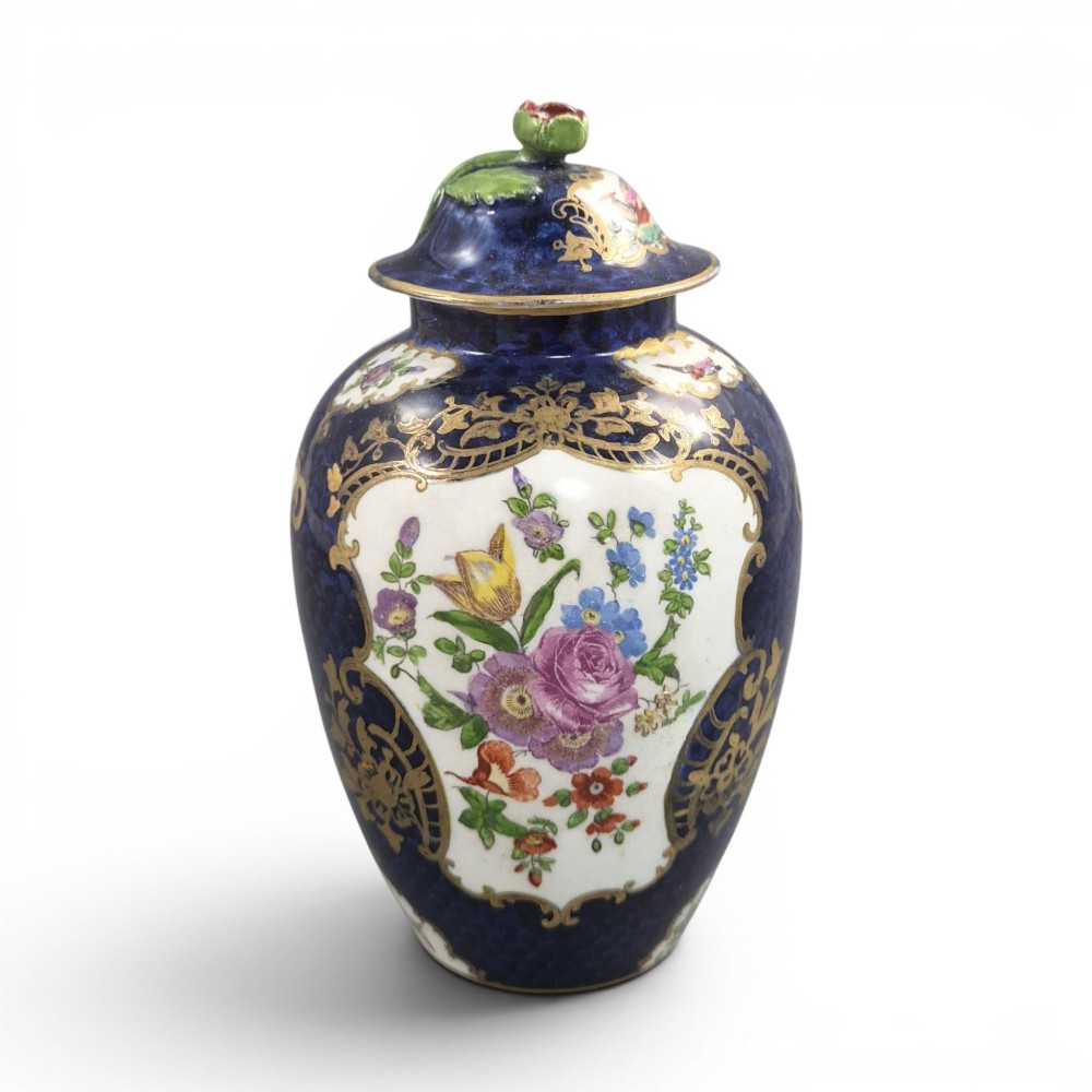 An Edwardian covered ceramic vase featuring a dark scale blue ground with gilded rococo cartouches framing painted floral panels.
