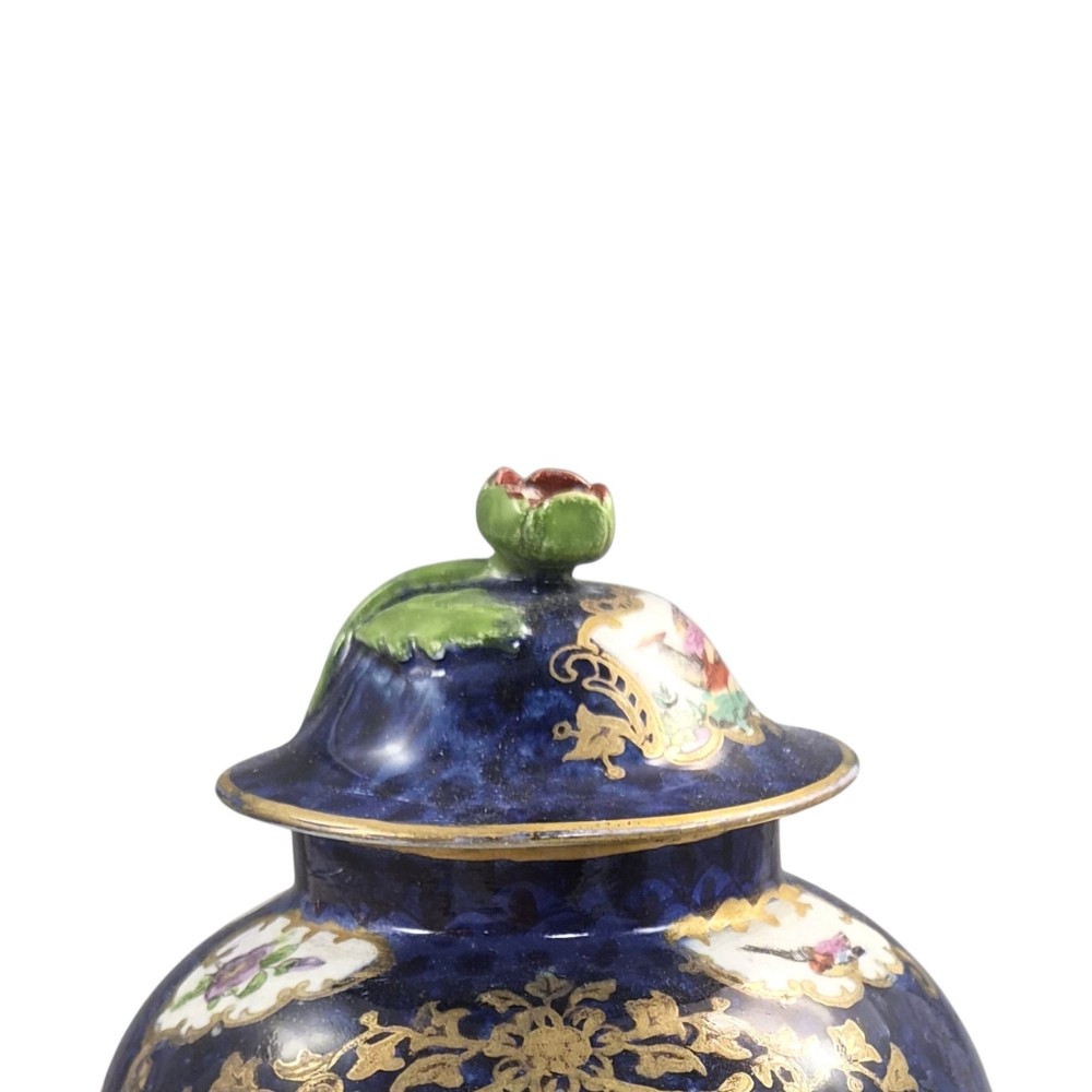 An Edwardian covered ceramic vase featuring a dark scale blue ground with gilded rococo cartouches framing painted floral panels. View IV