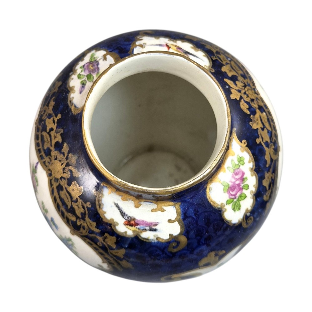 An Edwardian covered ceramic vase featuring a dark scale blue ground with gilded rococo cartouches framing painted floral panels. View VI