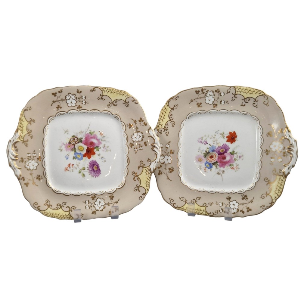 A pair of early Victorian Coalport porcelain square dessert dishes featuring hand-painted floral centres, beige borders with gold scrollwork, and moulded twin handles. View II