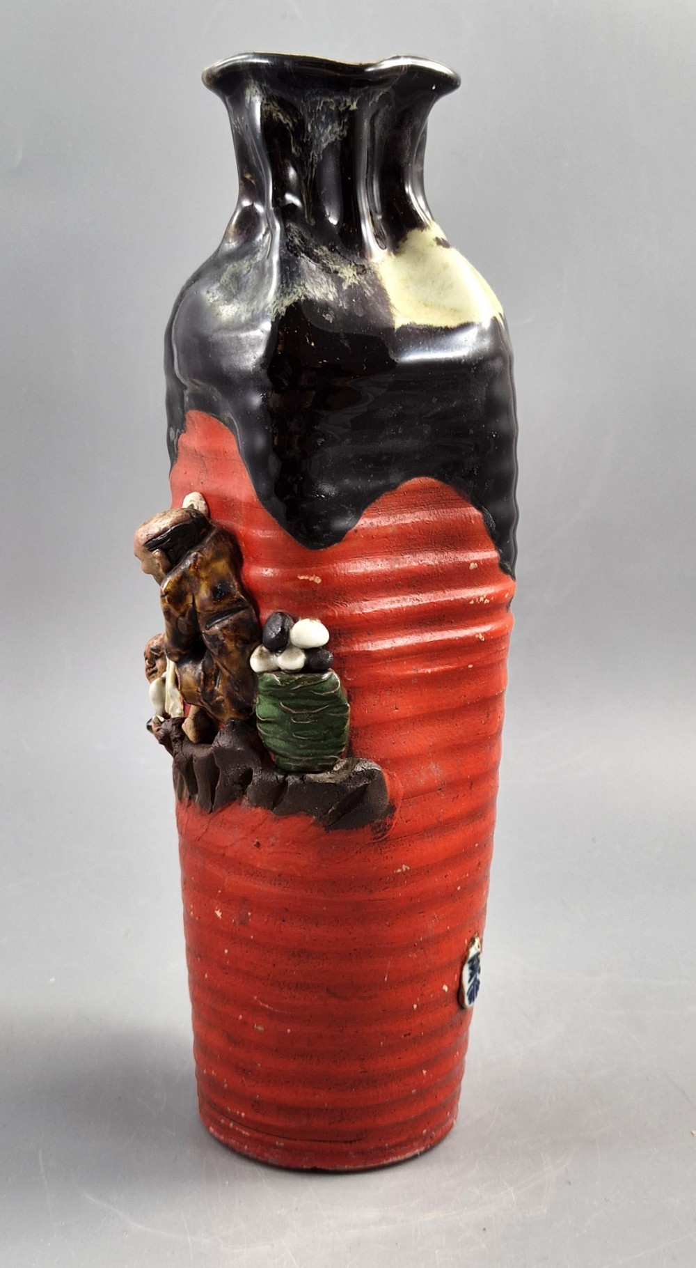 A tall Japanese Sumida Gawa ceramic vase featuring a ribbed red base, applied relief figures of sages on a cliff, and a heavy dark drip glaze around the rim. View II