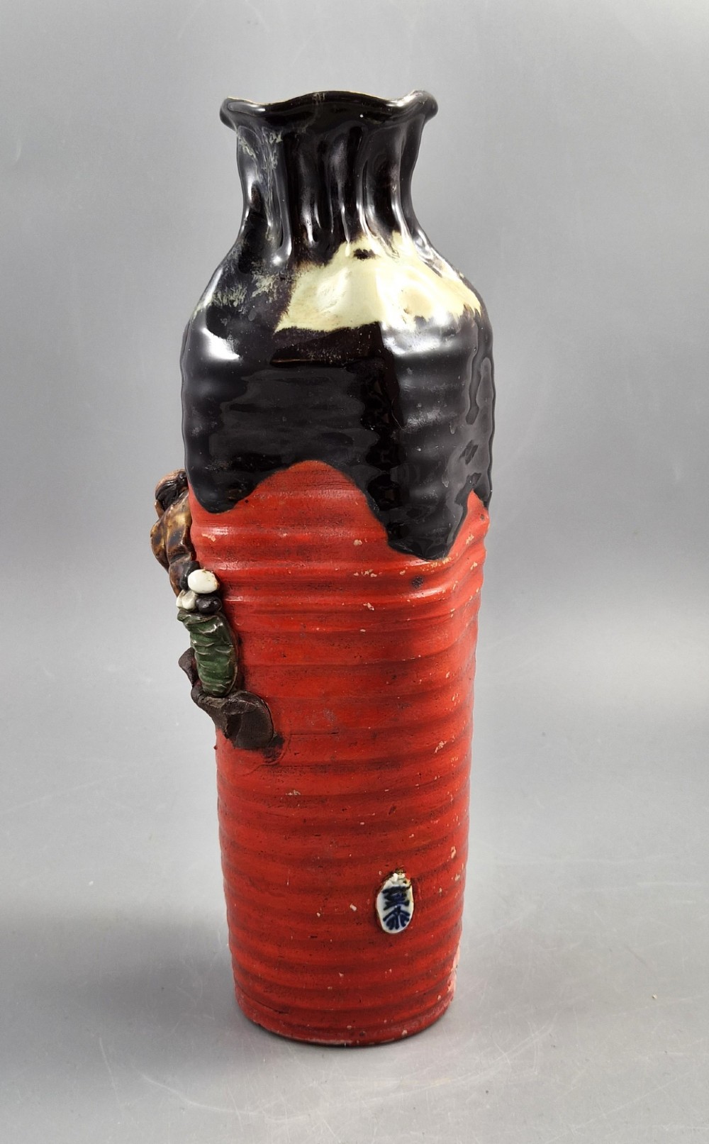 A tall Japanese Sumida Gawa ceramic vase featuring a ribbed red base, applied relief figures of sages on a cliff, and a heavy dark drip glaze around the rim. View III