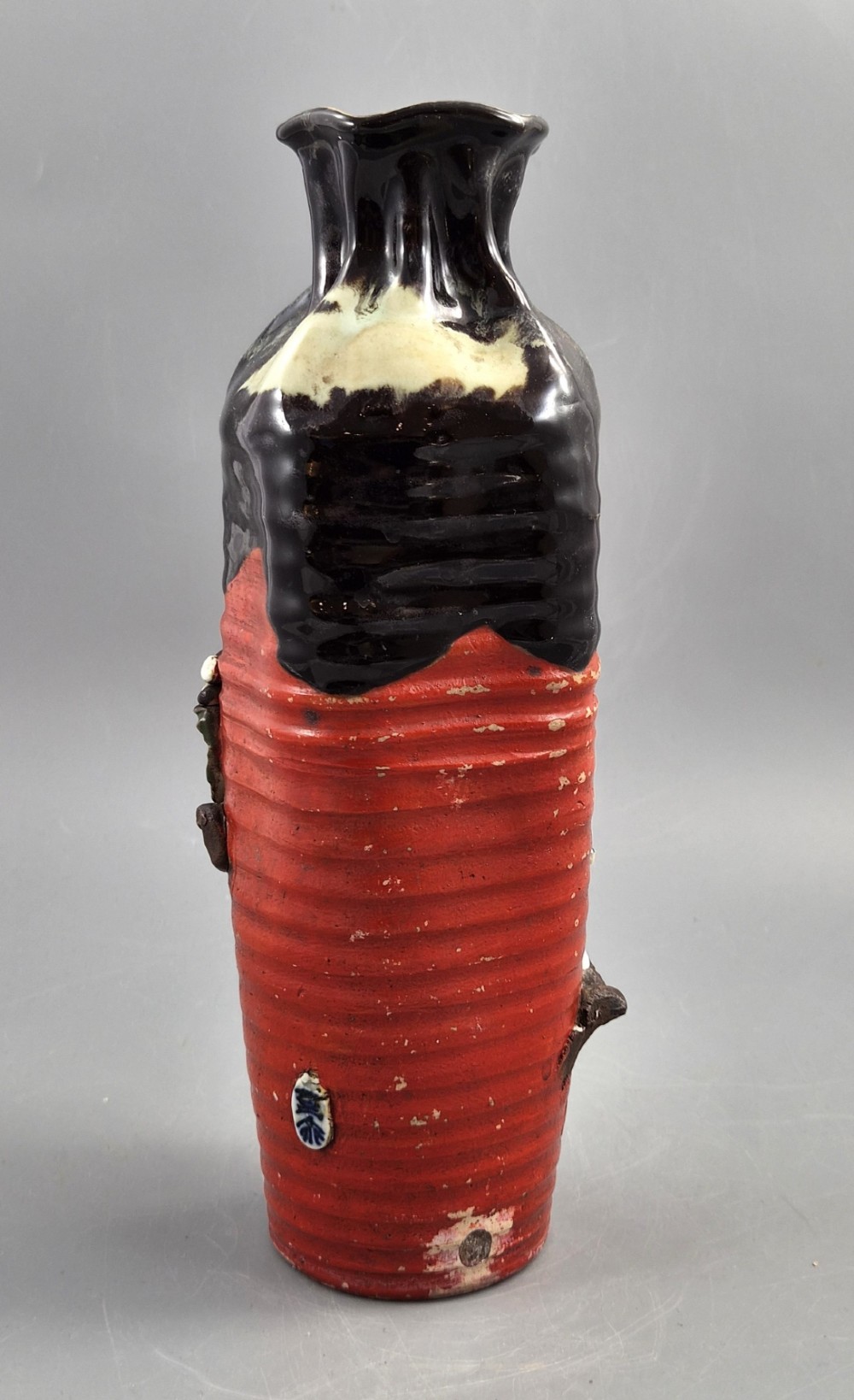 A tall Japanese Sumida Gawa ceramic vase featuring a ribbed red base, applied relief figures of sages on a cliff, and a heavy dark drip glaze around the rim. View IV