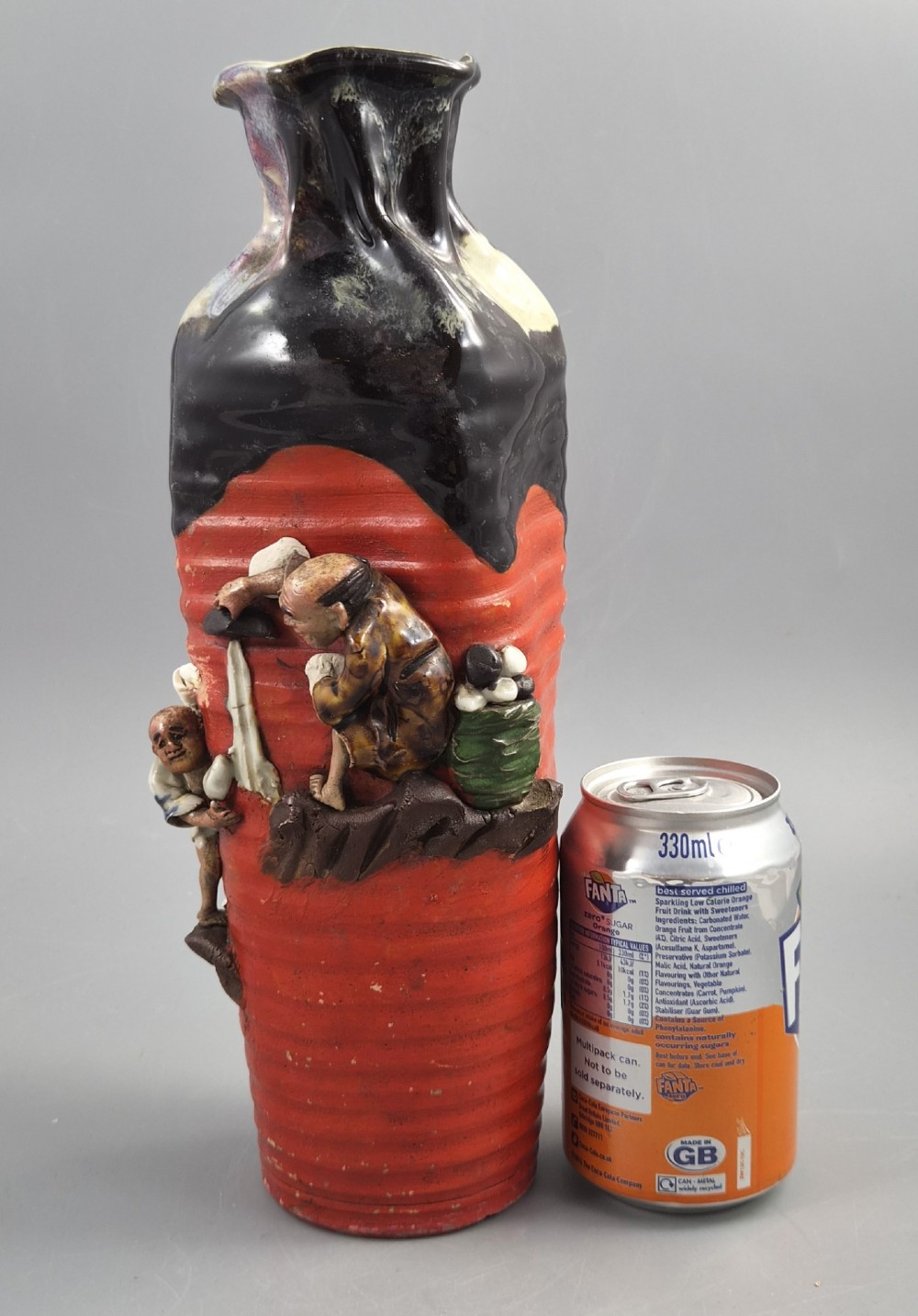 A tall Japanese Sumida Gawa ceramic vase featuring a ribbed red base, applied relief figures of sages on a cliff, and a heavy dark drip glaze around the rim. View XII