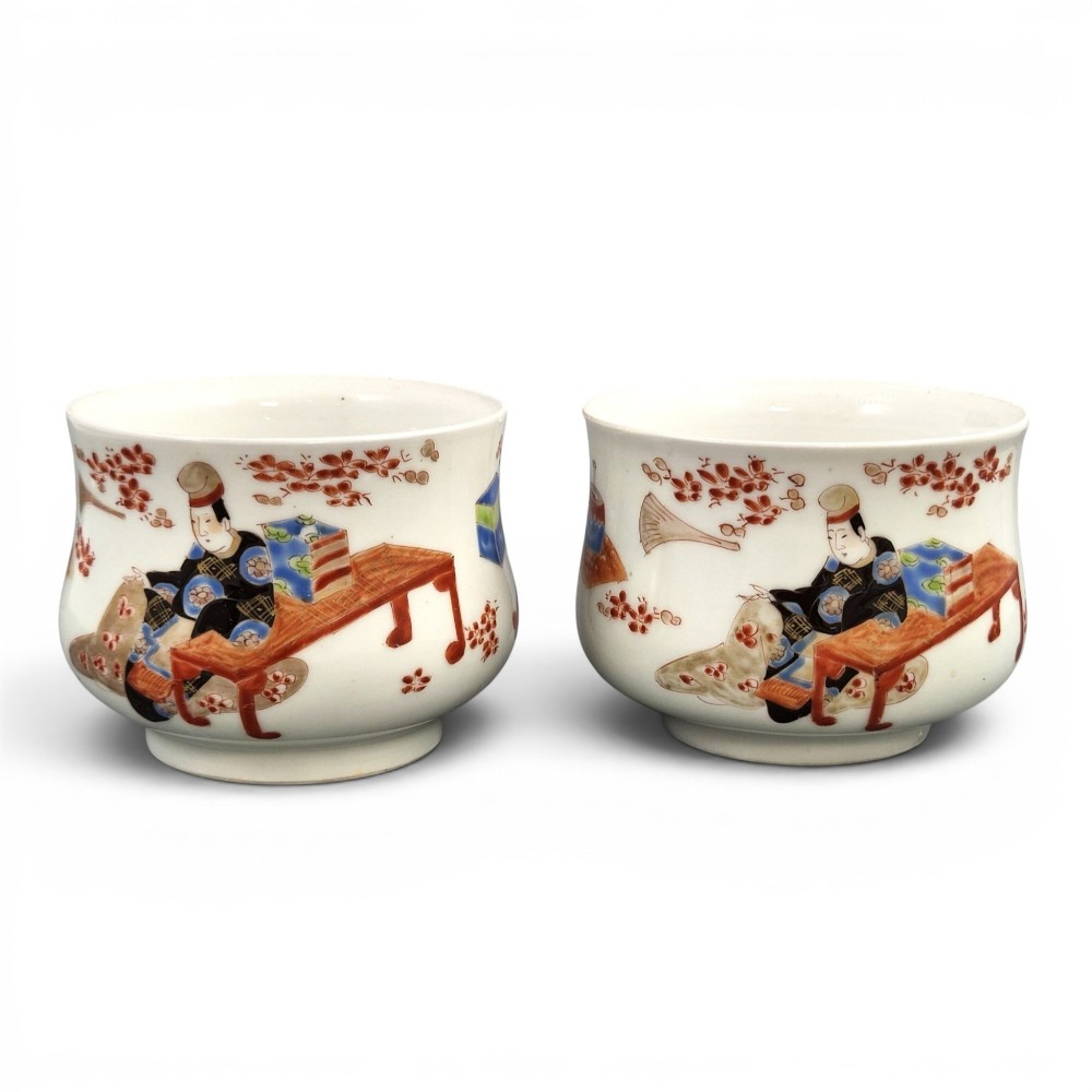 A pair of late 19th-century white Japanese Imari porcelain handleless sencha teacups hand-painted with figures at low desks and floral motifs in iron red and black enamels.