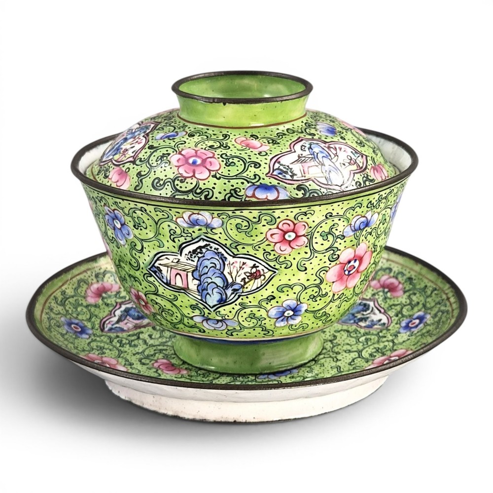 A Chinese Canton enamel gaiwan featuring a green ground with pink floral scrolls and landscape cartouches, complete with lid and matching saucer.