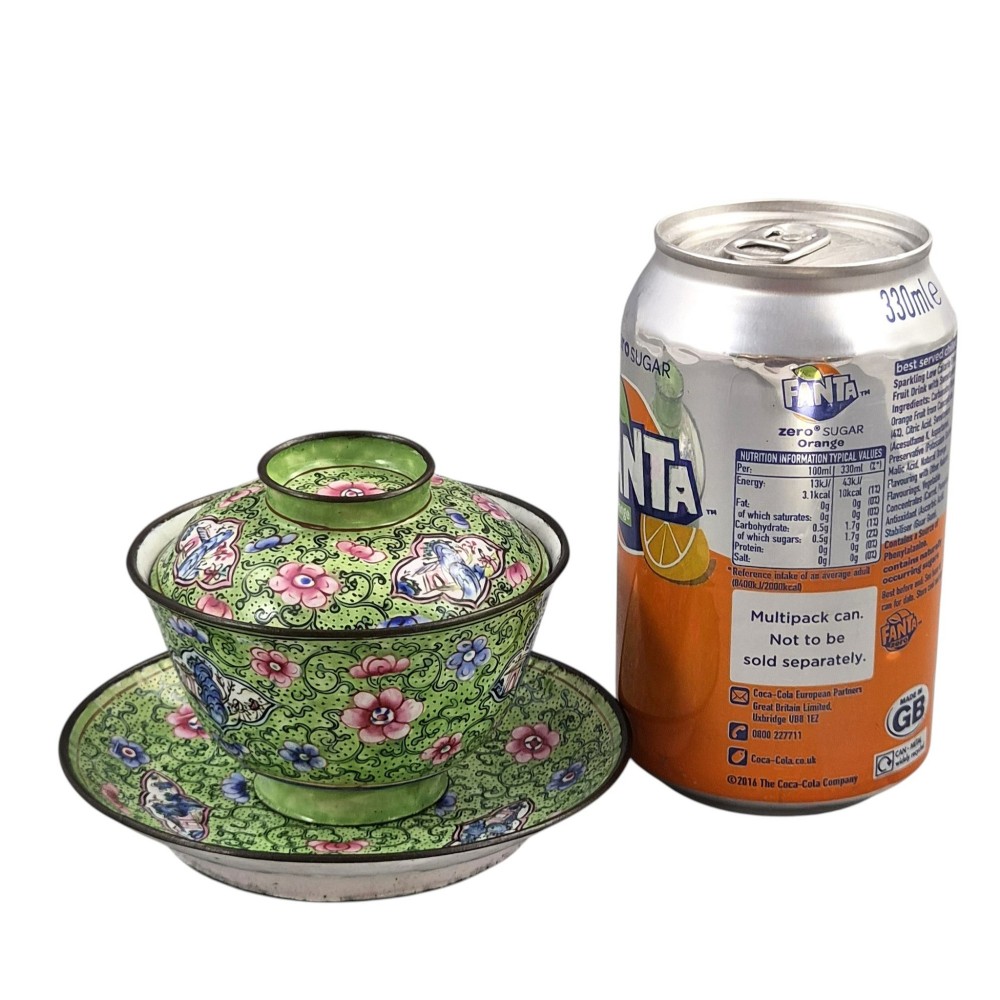 A Chinese Canton enamel gaiwan featuring a green ground with pink floral scrolls and landscape cartouches, complete with lid and matching saucer. View XV