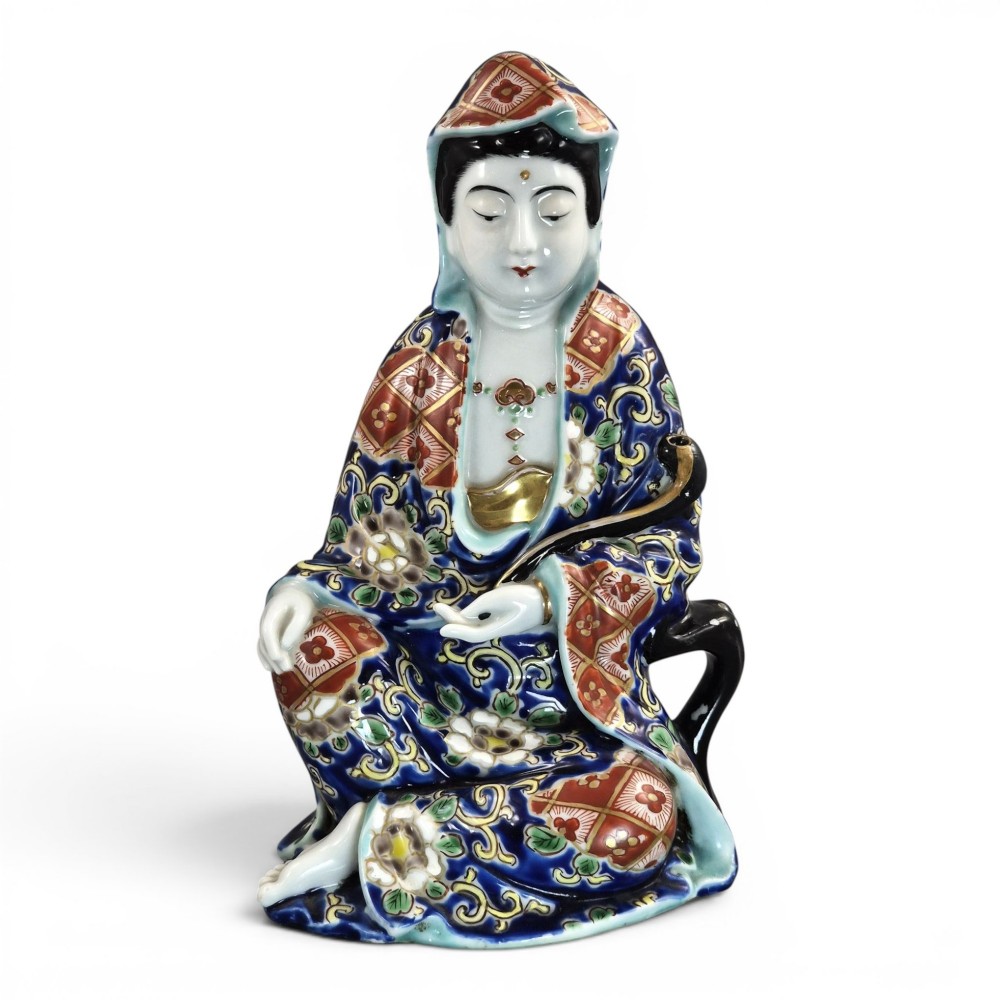 A seated Japanese Arita porcelain figure depicting Jigoku Dayu wearing a patterned blue, red, and gold hooded robe.