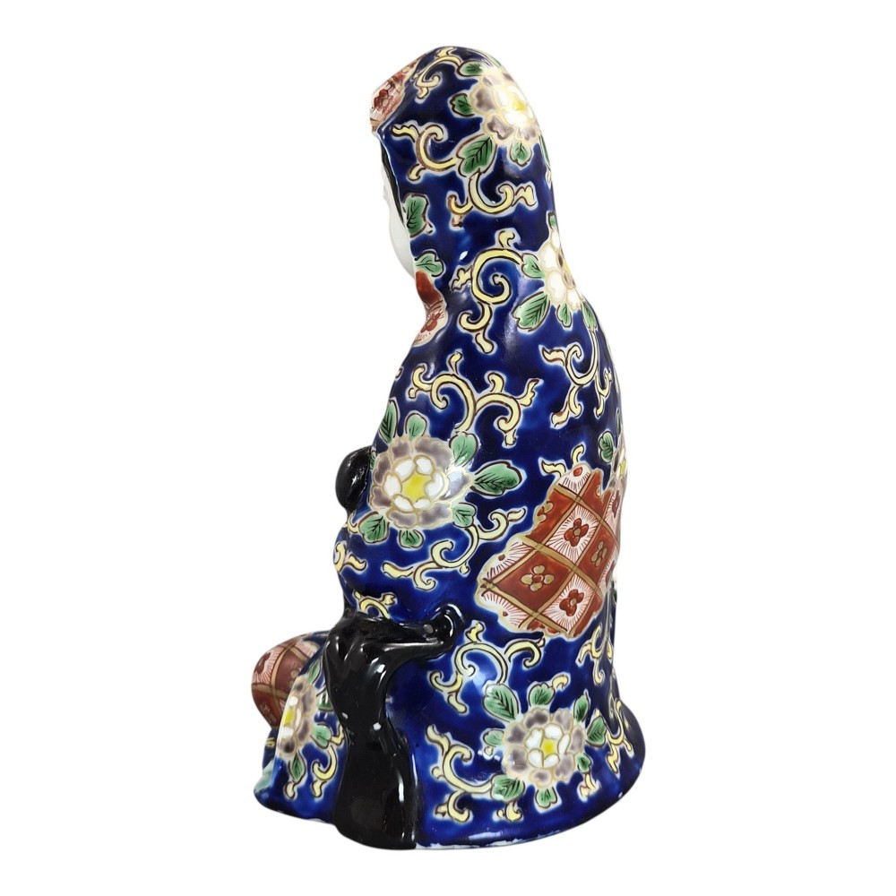 A seated Japanese Arita porcelain figure depicting Jigoku Dayu wearing a patterned blue, red, and gold hooded robe. View III