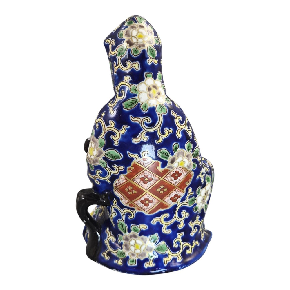 A seated Japanese Arita porcelain figure depicting Jigoku Dayu wearing a patterned blue, red, and gold hooded robe. View IV