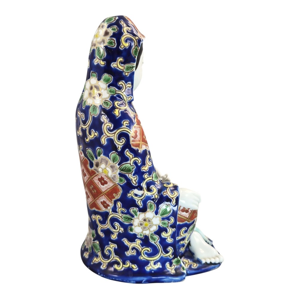 A seated Japanese Arita porcelain figure depicting Jigoku Dayu wearing a patterned blue, red, and gold hooded robe. View V