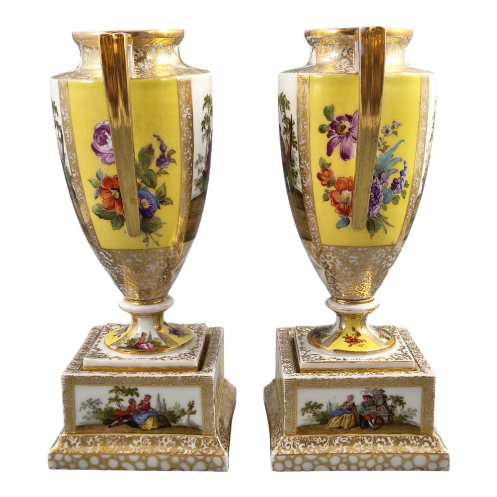 A pair of late nineteenth-century Dresden porcelain urns featuring yellow ground, hand-painted romantic scenes, gilded handles, and square pedestal bases. View II