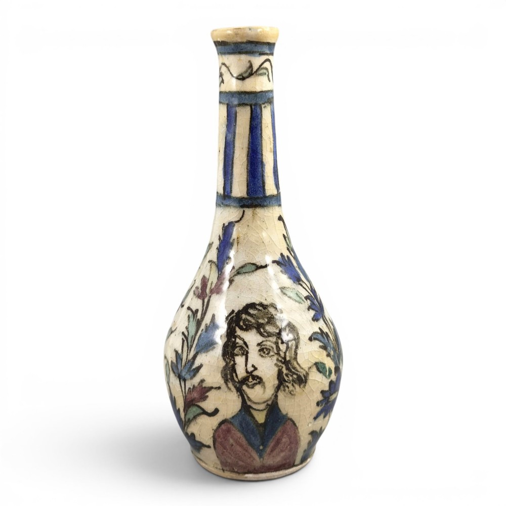 An Iranian Qajar ceramic bottle vase featuring an elongated neck, cream crackle glaze, and hand-painted blue and purple figurative portrait and floral motifs.
