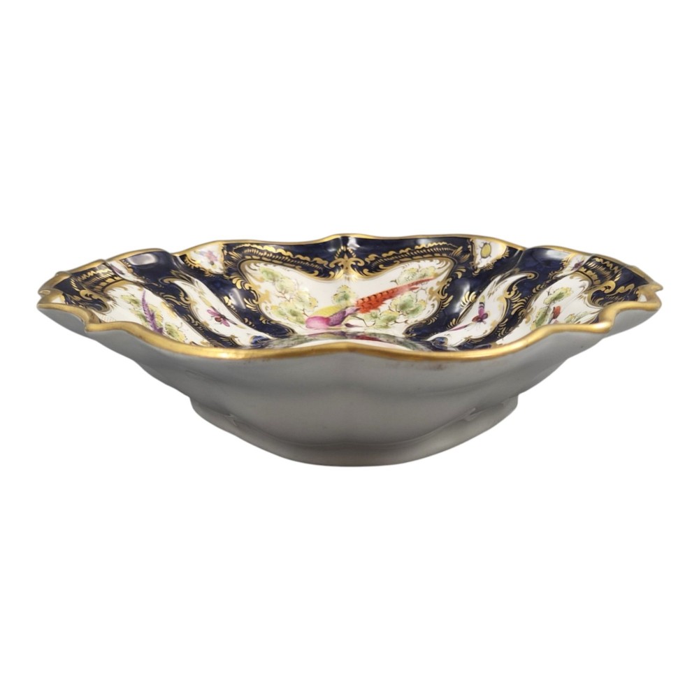 An oval scalloped porcelain dessert dish featuring a deep blue scale ground pattern with gilt-framed reserves containing hand-painted exotic birds and insects. View VII