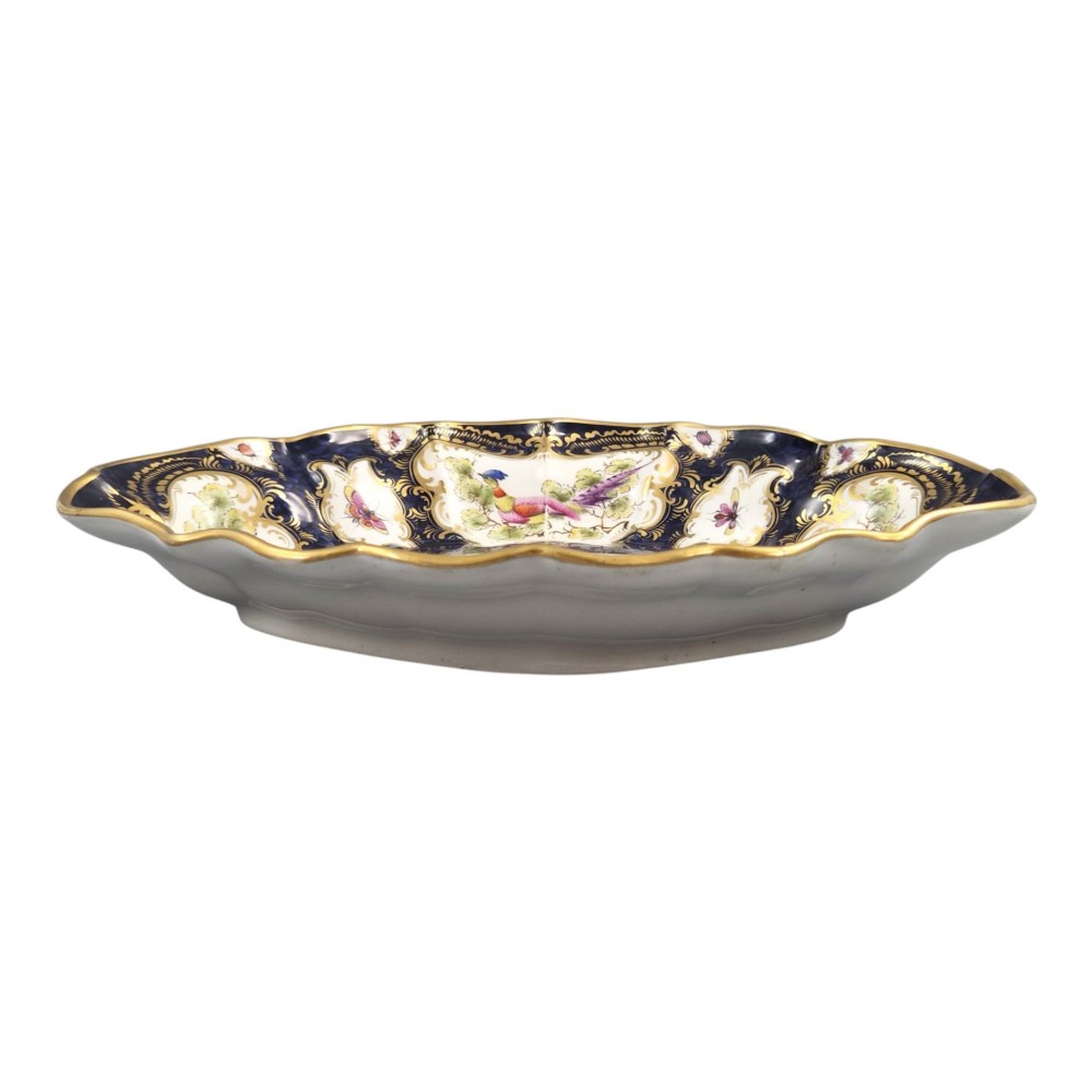 An oval scalloped porcelain dessert dish featuring a deep blue scale ground pattern with gilt-framed reserves containing hand-painted exotic birds and insects. View VIII