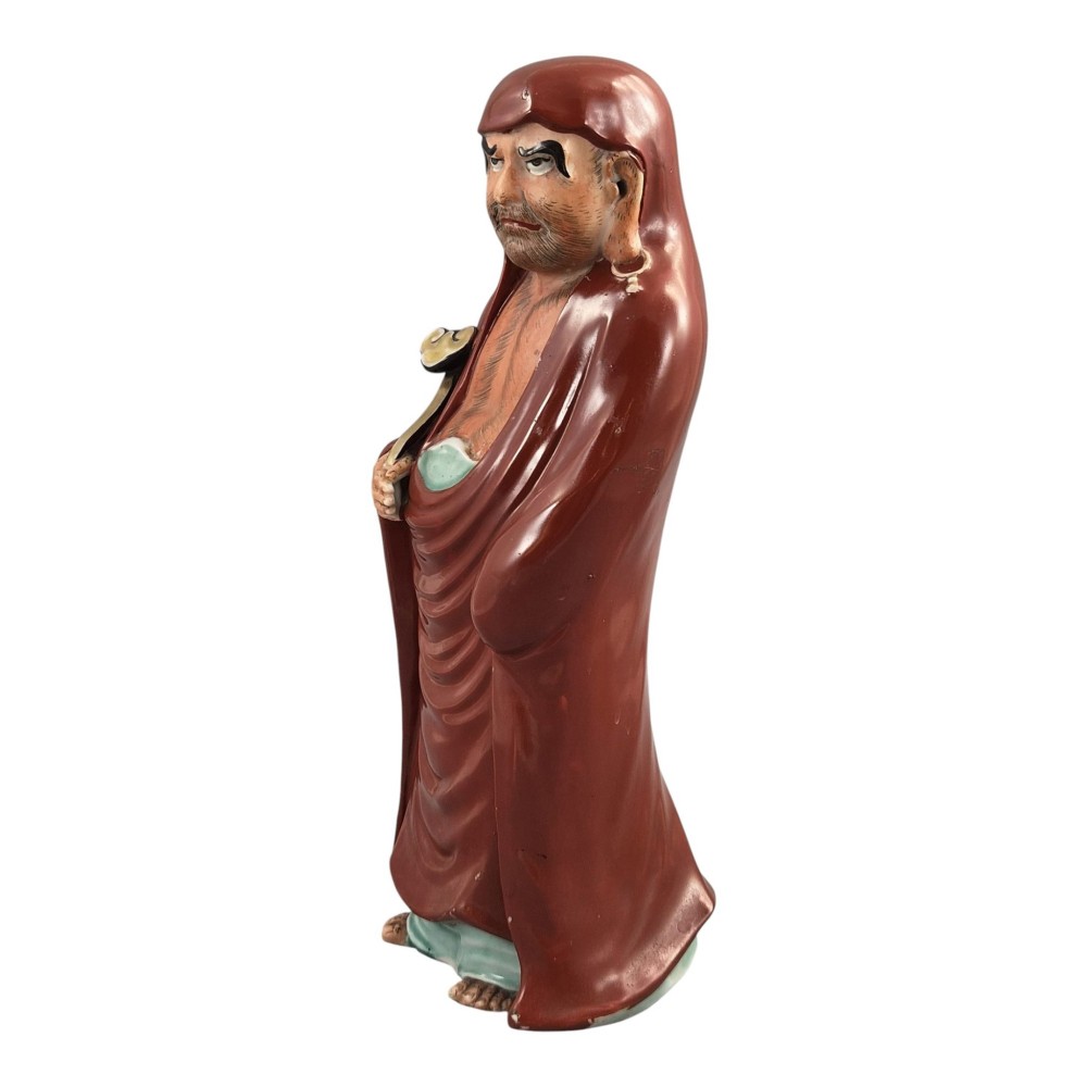 A standing Japanese Kutani porcelain okimono figure depicting Bodhidharma wearing draped terracotta red robes and holding a sceptre. View II