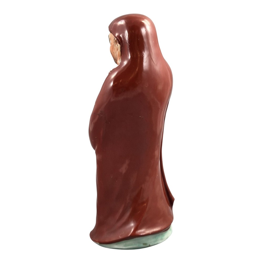 A standing Japanese Kutani porcelain okimono figure depicting Bodhidharma wearing draped terracotta red robes and holding a sceptre. View III