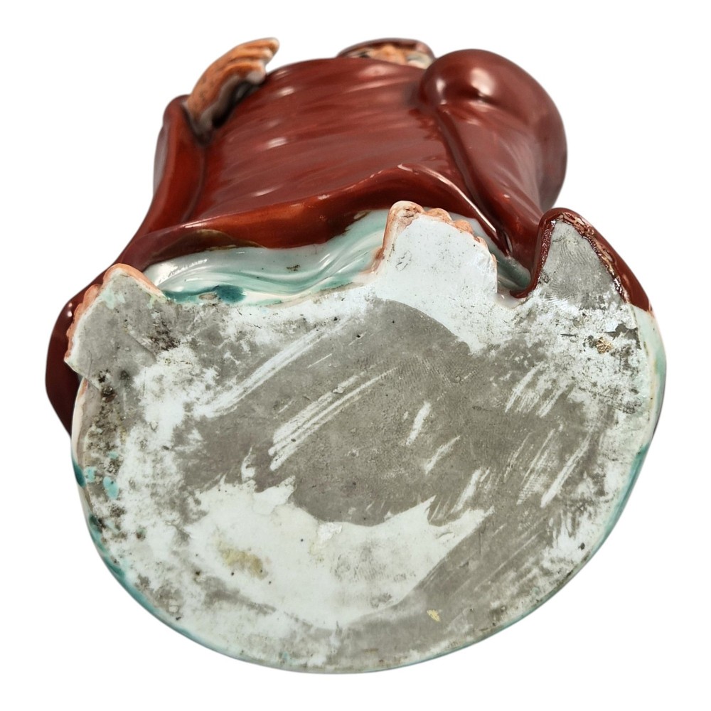 A standing Japanese Kutani porcelain okimono figure depicting Bodhidharma wearing draped terracotta red robes and holding a sceptre. View VII