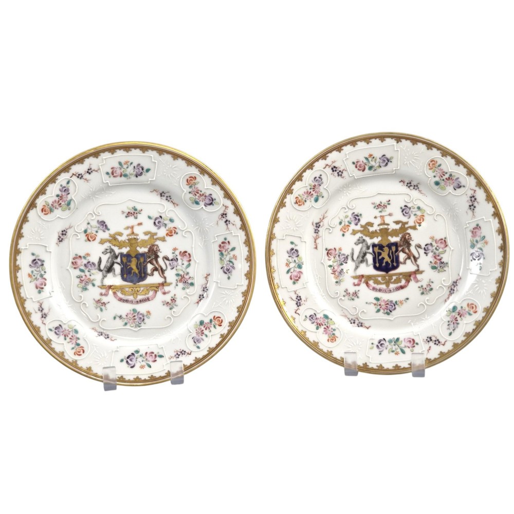 A pair of circular white porcelain plates featuring a central coat of arms, hand-painted floral sprays, raised enamel details, and gilded rims.