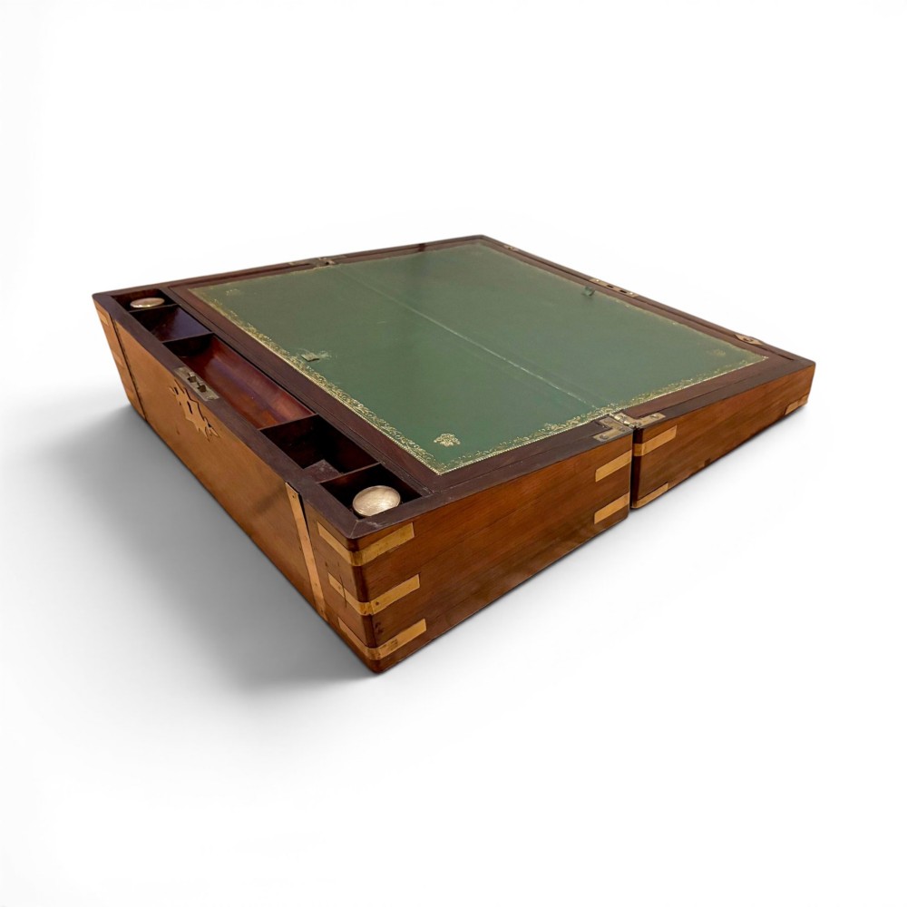 An open Victorian mahogany writing slope featuring flush brass corner bindings, internal pen compartments, and a green gilt-tooled leather writing surface.