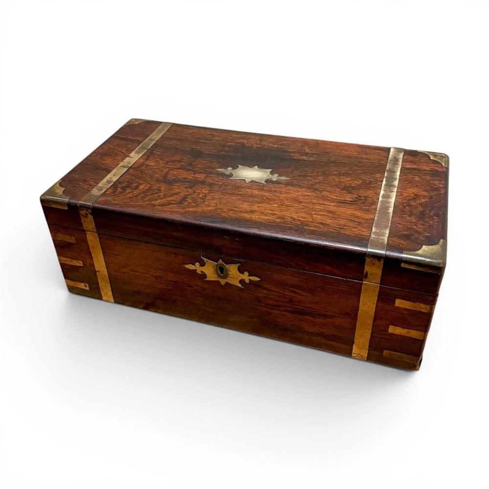 A closed rectangular Victorian rosewood writing slope featuring brass strapping, brass corner mounts, and a central brass escutcheon.