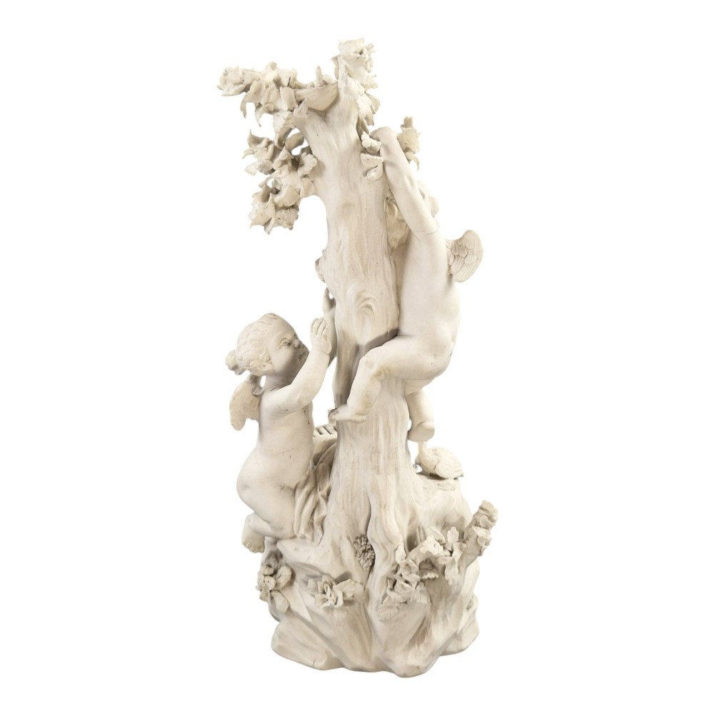 An unglazed off-white biscuit porcelain figure depicting two winged cherubs beside a tree trunk with a birdcage near the base. View IV