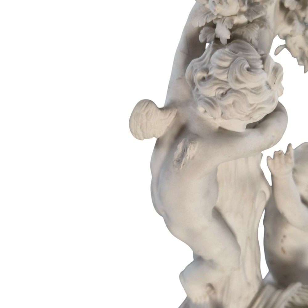 An unglazed off-white biscuit porcelain figure depicting two winged cherubs beside a tree trunk with a birdcage near the base. View VIII