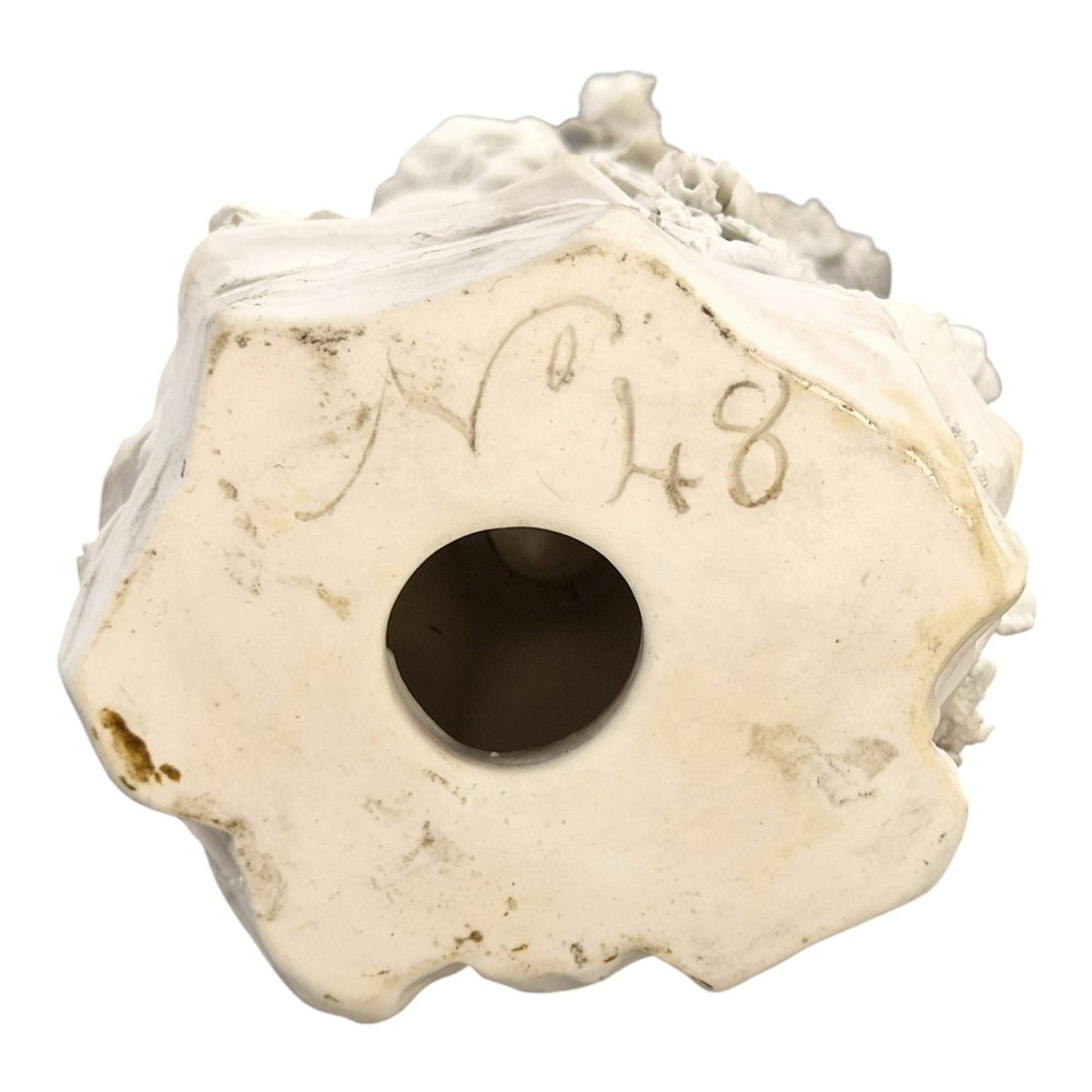 An unglazed off-white biscuit porcelain figure depicting two winged cherubs beside a tree trunk with a birdcage near the base. View IX