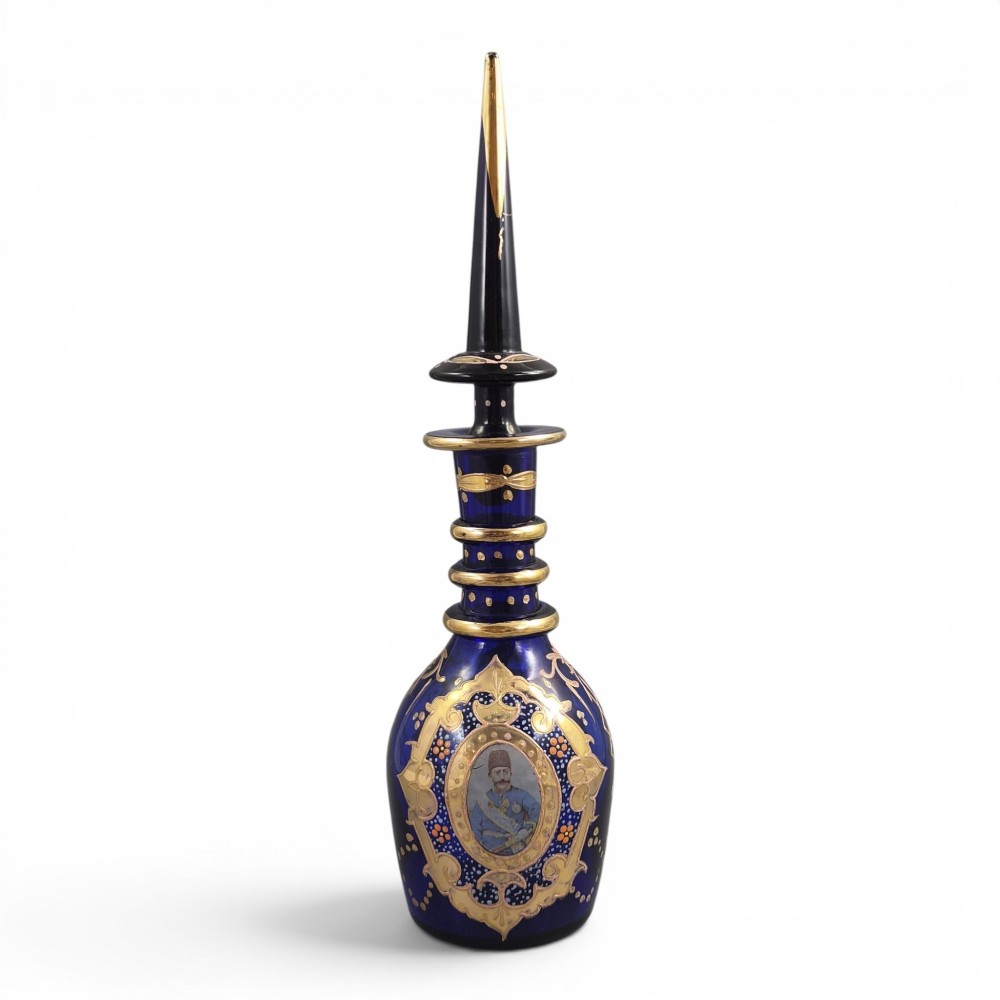 A cobalt blue Bohemian glass decanter decorated with elaborate gold enamelling and a painted portrait medallion, featuring a tall pointed stopper.