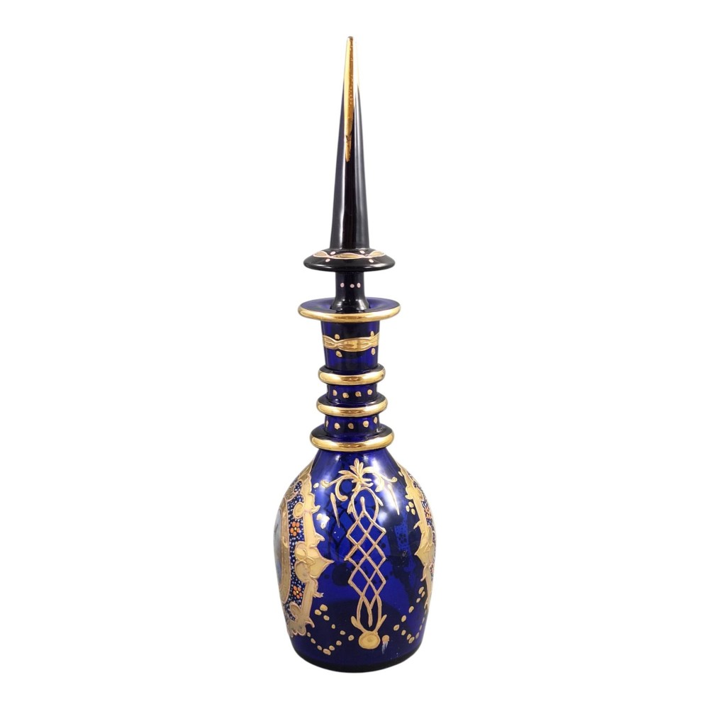 A cobalt blue Bohemian glass decanter decorated with elaborate gold enamelling and a painted portrait medallion, featuring a tall pointed stopper. View IV